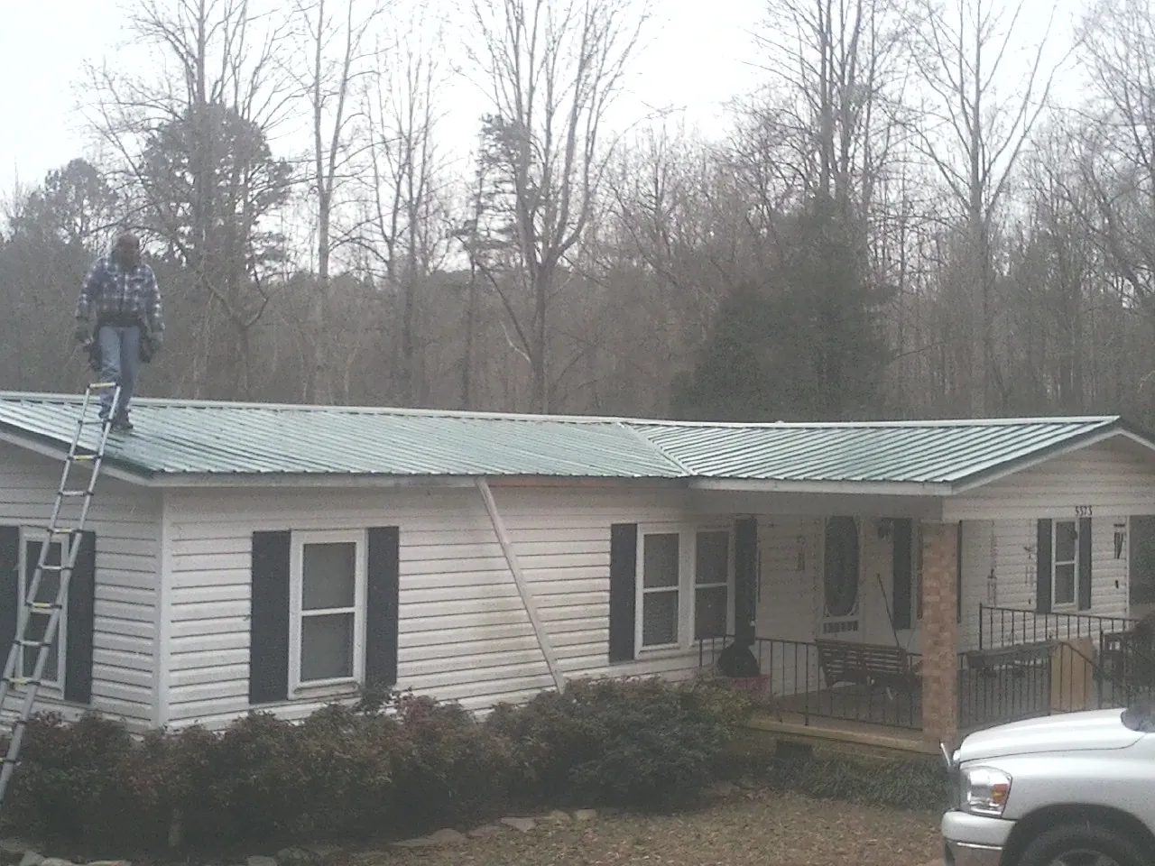 Worker on a ladder beside a new green metal roof on a ranch home in Rosendale