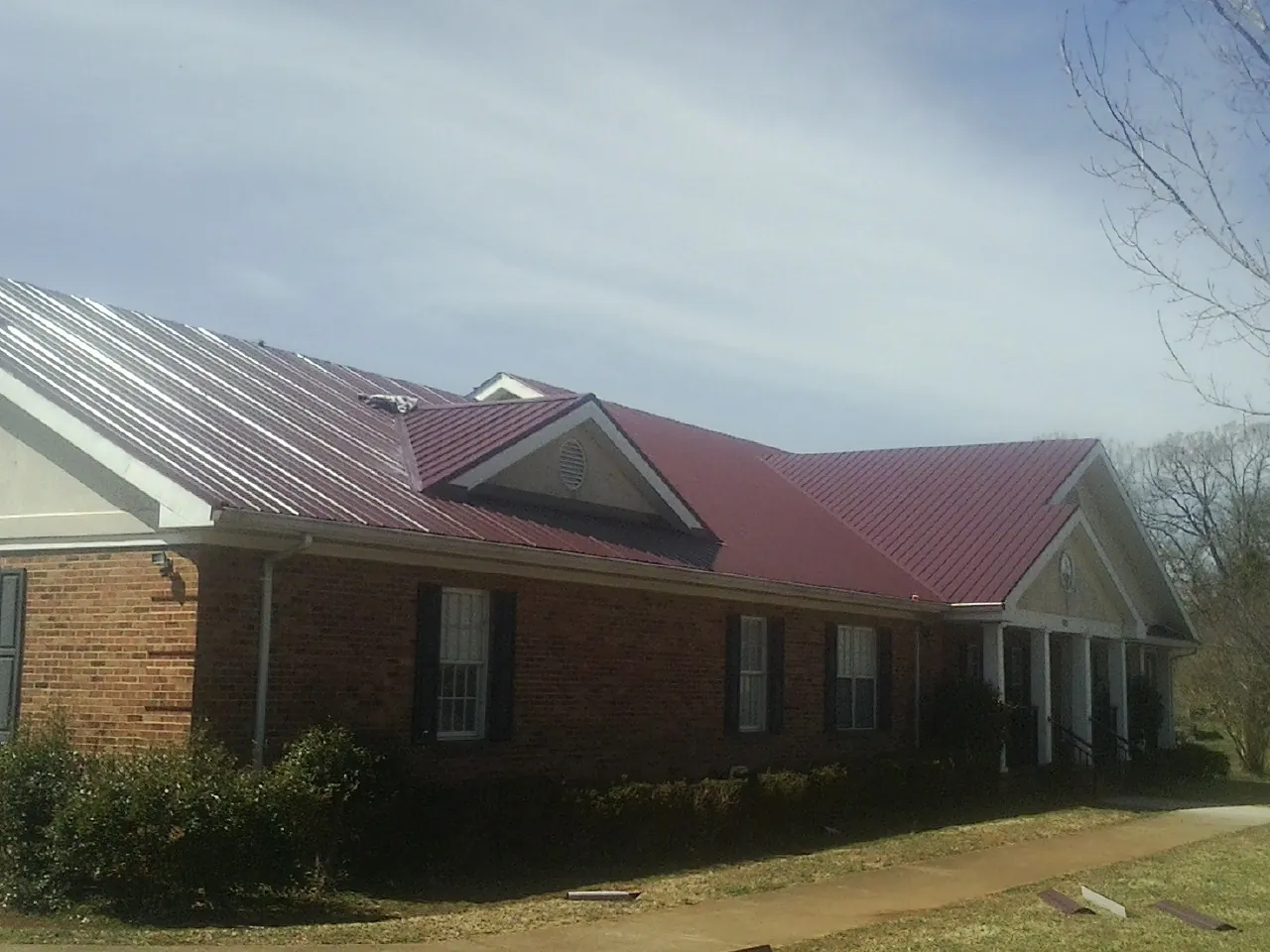Red metal roof with gabled entries on a long brick building, from a Hail Damage Roof Repair job in Rosendale