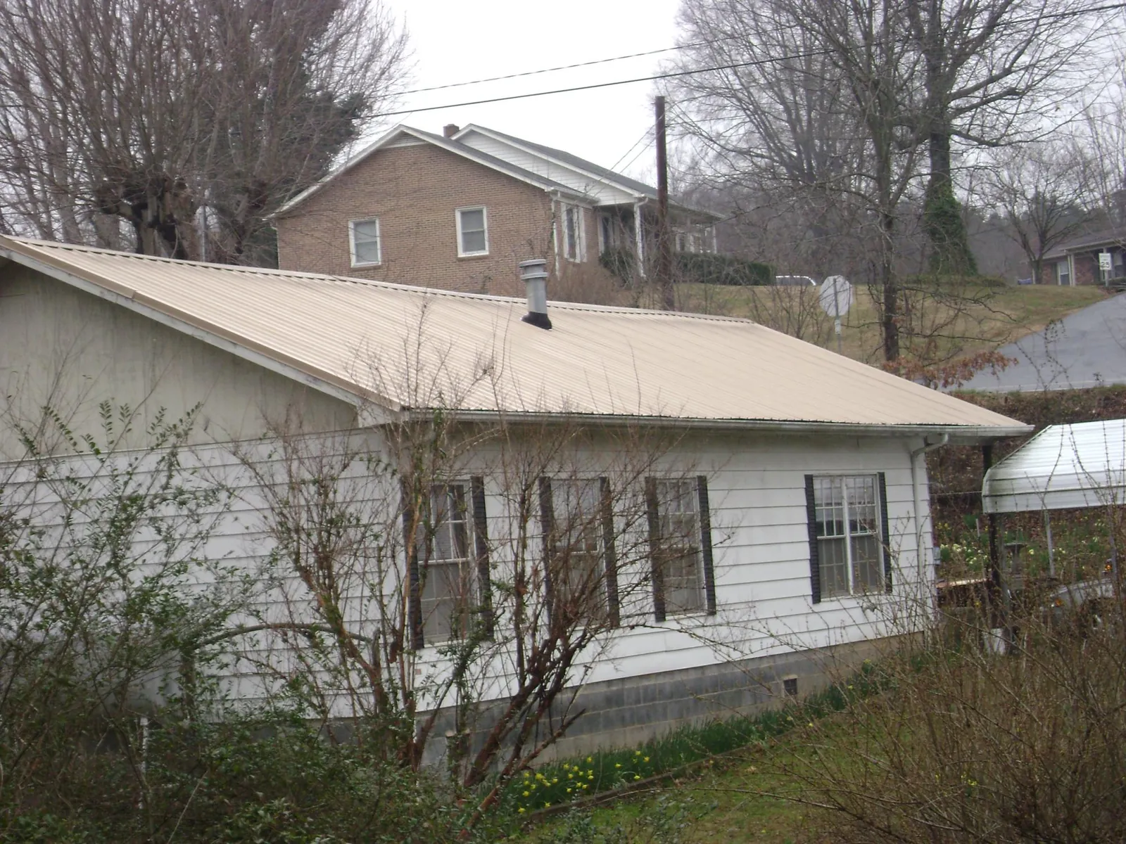 Tan metal roof on a white sided house set into a hillside — Commercial Roofing by Roofing Brothers in Rosendale